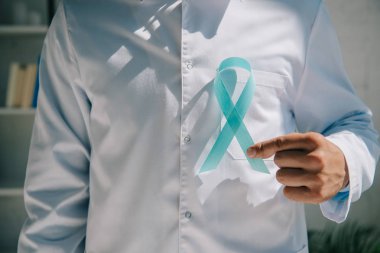 Mavi farkındalık kurdelesi taşıyan beyaz önlüklü bir doktor. 