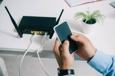 cropped view of businessman holding smartphone near plugged router clipart