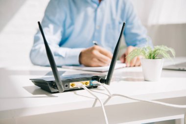 selective focus of plugged router near businessman writing in notebook clipart