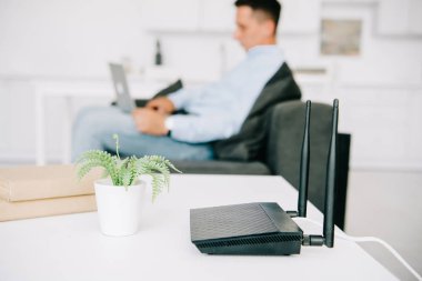 selective focus of black router on white desk near flowerpot and businessman using laptop clipart