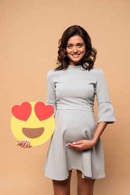 Kyiv, Ukrayna - 1 Ağustos 2019: bej arka planda kalbi olan gri elbiseli hamile bir kadın. 