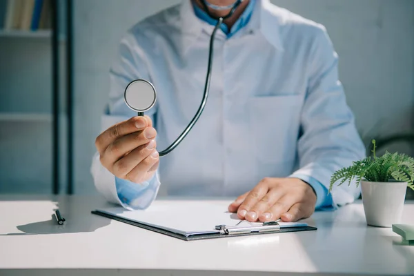 Vista Cortada Médico Segurando Estetoscópio Enquanto Sentado Mesa — Fotografia de Stock