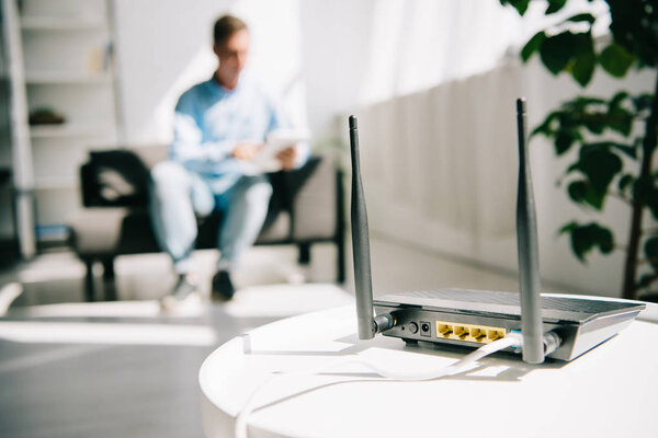 selective focus of black plugged router on white table and businessman sitting on sofa