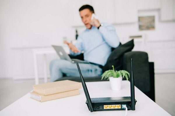 selective focus of black plugged router on white table and businessman talking on smartphone