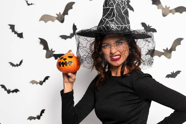 angry woman in witch hat holding pumpkin in Halloween