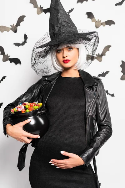 pregnant woman in witch hat and wig holding pot with candies in Halloween