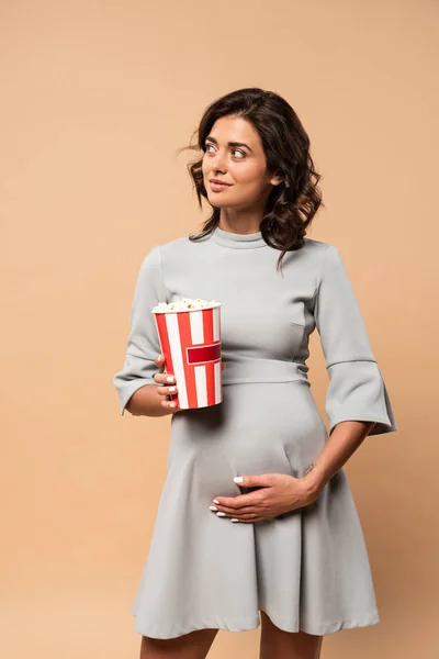 Ciężarna Kobieta Szarej Sukience Dotykająca Brzucha Trzymająca Popcorn Beżowym Tle — Zdjęcie stockowe