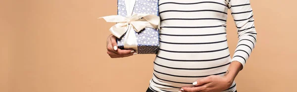 ベージュを背景に妊娠中の女性がプレゼントを持つ — ストック写真