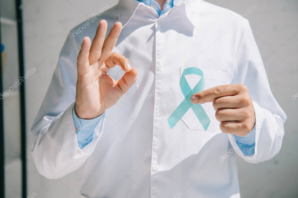 cropped view of doctor holding blue awareness ribbon and showing ok sign