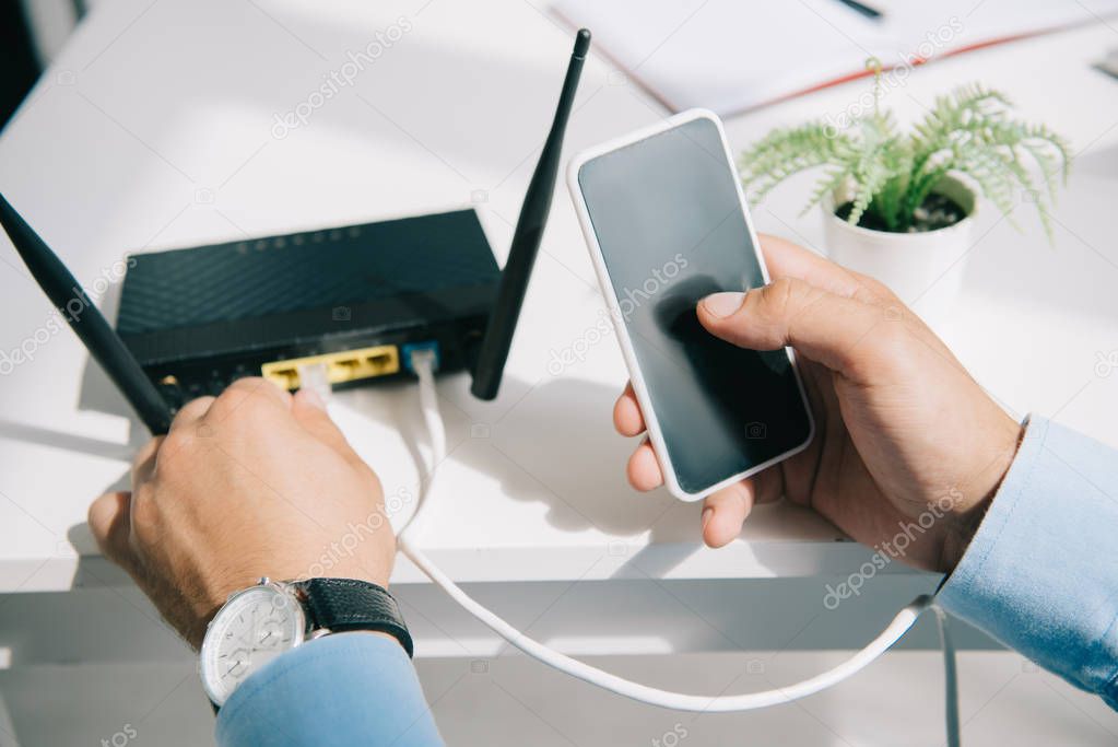 cropped view of businessman plugging router while holding smartphone