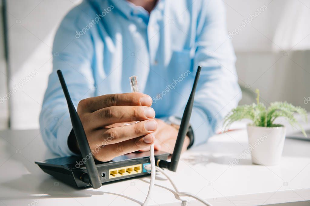 selective focus of businessman holding wire with connector near router
