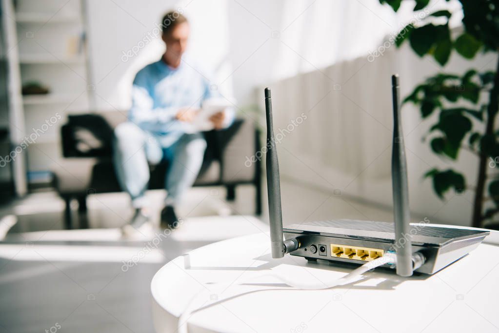 selective focus of black plugged router on white table and businessman sitting on sofa