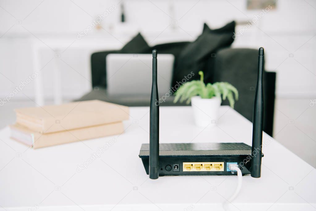 black plugged router on white table near books and flowerpot