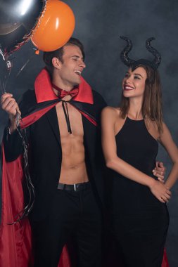 Vampir cadılar bayramı kostümlü mutlu adam boynuzları siyah dumanlı kızın yanında balon tutuyor. 