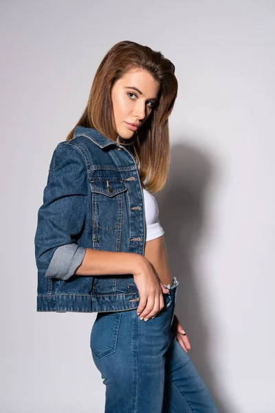 pretty young woman in denim jacket standing on white