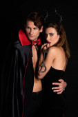 schöner Mann in Mantel umarmt Frau mit Hörnern hält Handschellen isoliert auf schwarz 