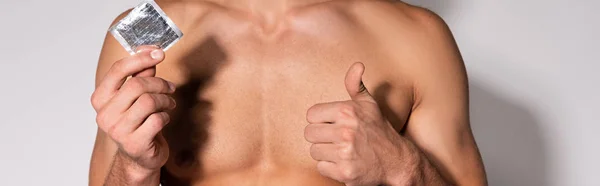 Панорамный Снимок Мускулистого Мужчины Показывающего Большой Палец Вверх Держа Презерватив — стоковое фото