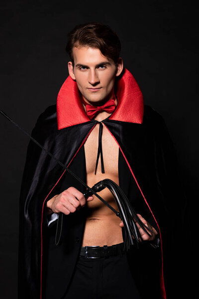 handsome man in vampire halloween costume holding flogging whip isolated on black 