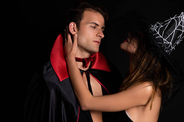 woman in witch hat touching face of man isolated on black 