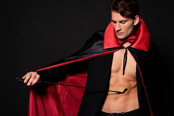 sexy man in vampire halloween costume holding flogging whip isolated on black 