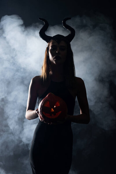 silhouette of woman with horns holding spooky pumpkin on black with smoke 