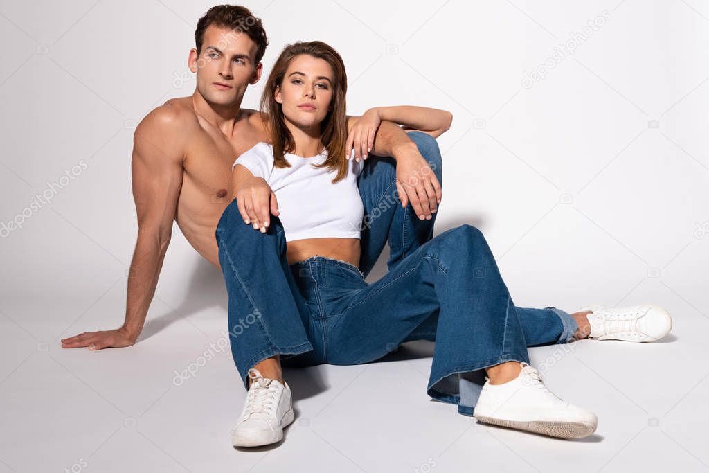 pretty woman in denim jeans sitting with sexy man on white 