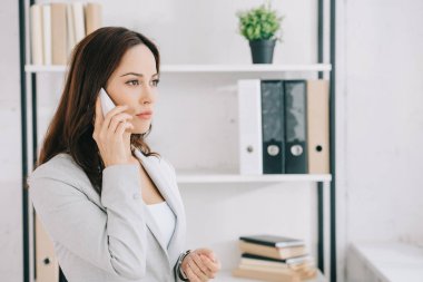 Ofiste akıllı telefonla konuşurken bakışlarını kaçıran çekici, düşünceli bir sekreter.