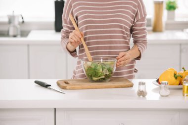 partial view of woman mixing fresh vegetable salad while standing at kitchen table