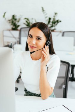 selective focus of cheerful broker touching headset while working in call center  clipart