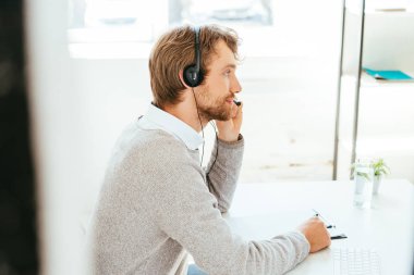 selective focus of handsome bearded operator in brokers agency touching headset  clipart