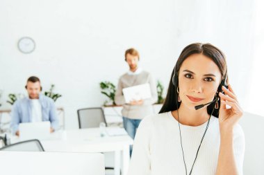 selective focus of beautiful broker touching headset while working with coworkers  clipart