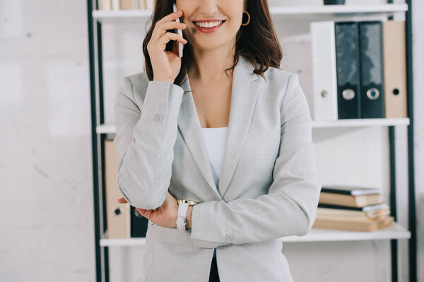 cropped view of smiling, elegant secretary talking on smartphone in office