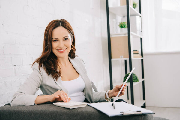 веселый молодой секретарь смотрит в камеру, сидя на диване в офисе
