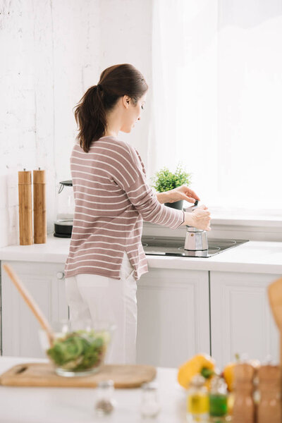 selective focus of young woman preparing coffee in geyser coffee maker