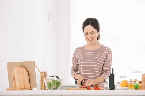 attractive, cheerful woman cutting fresh vegetables on chopping board