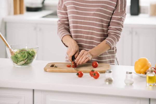 cropped view of woman cutting cheery tomatoes on chopping board