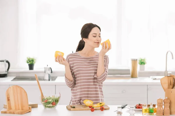 Mooie Jonge Vrouw Ruiken Gesneden Paprika Terwijl Staande Aan Keukentafel — Stockfoto