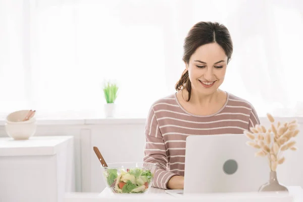 Junge Glückliche Frau Mit Laptop Küchentisch Neben Schüssel Mit Gemüsesalat — Stockfoto