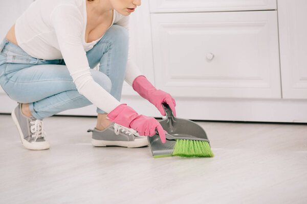 cropped view of young housewife sweeping floor with brush and scoop