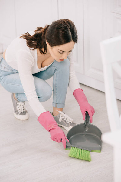 young housewife sweeping floor in kitchen with brush and scoop