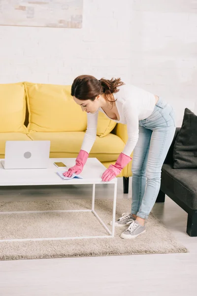 Jong Huisvrouw Spijkerbroek Vegen Tafel Met Doek Buurt Laptop — Stockfoto