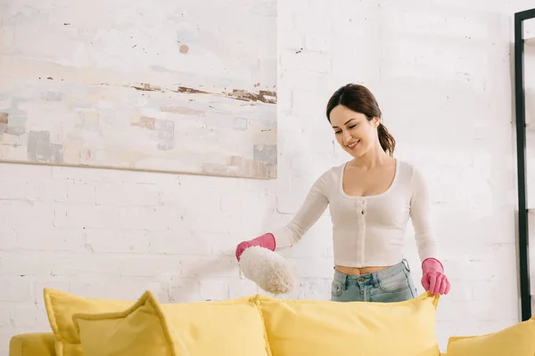 Atractiva Ama Casa Sonriendo Mientras Limpia Sofá Con Cepillo Polvo —  Fotos de Stock