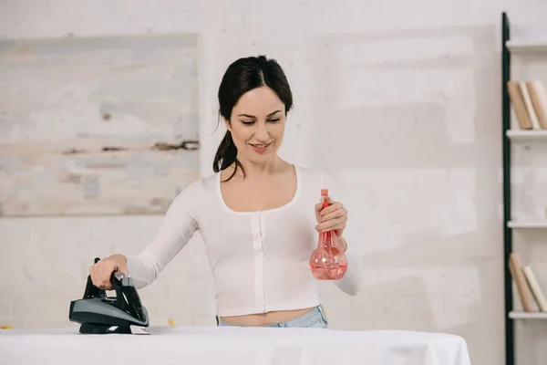 Smiling Housewife Holding Spray Bottle Holding Iron While Standing Ironing — Stock Photo, Image