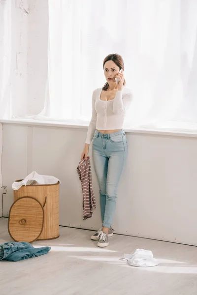 Attractive Housewife Talking Smartphone While Standing Laundry Basket Holding Clothes — Stock Photo, Image