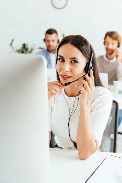 selective focus of attractive broker touching headset near coworkers in office 