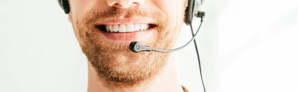 панорамный снимок бородатого брокера в наушниках, улыбающегося в офисе
 