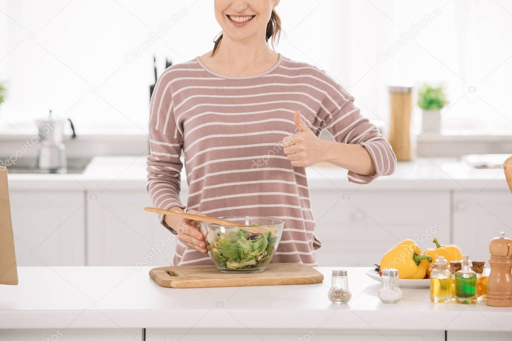 cropped view of smiling woman showing thumb up while standing near bowl with fresh vegetable salad 