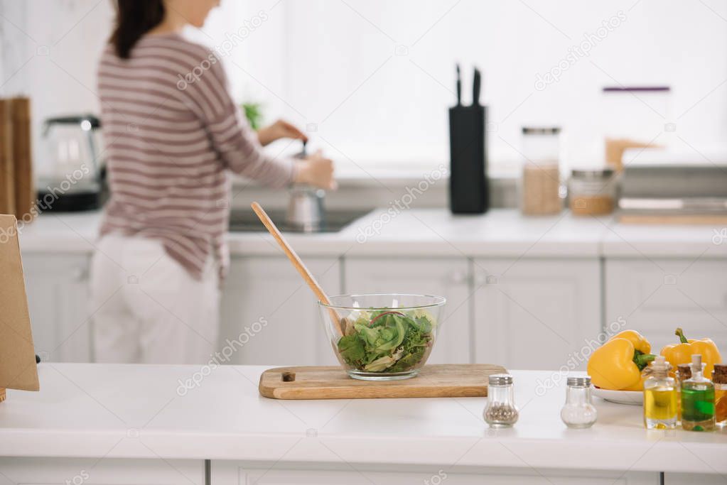 selective focus of bowl with fresh vegetable salad and woman preparing coffee in geyser coffee maker