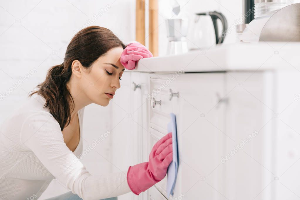 tired housewife with closed eyes washing kitchen furniture with rag