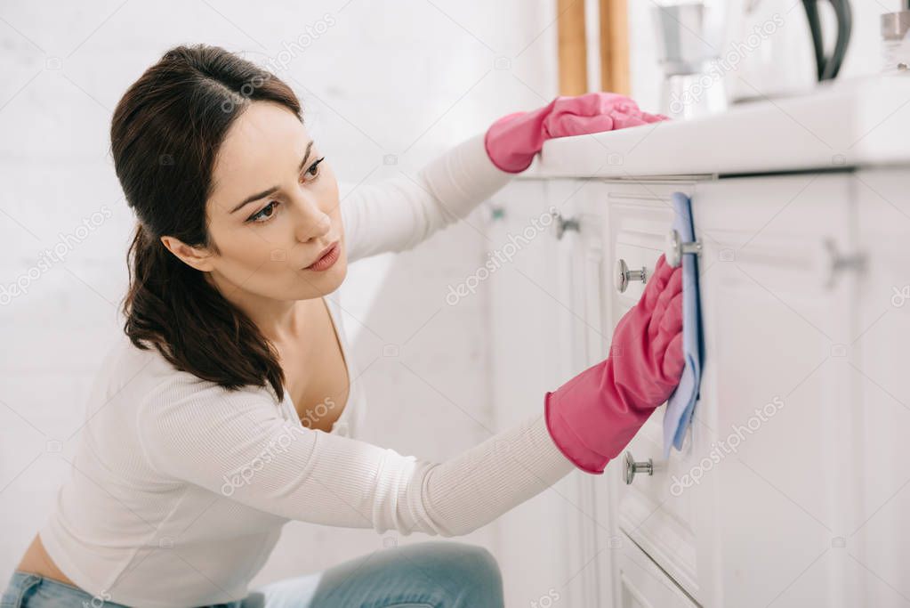 attractive housewife washing kitchen furniture with rag
